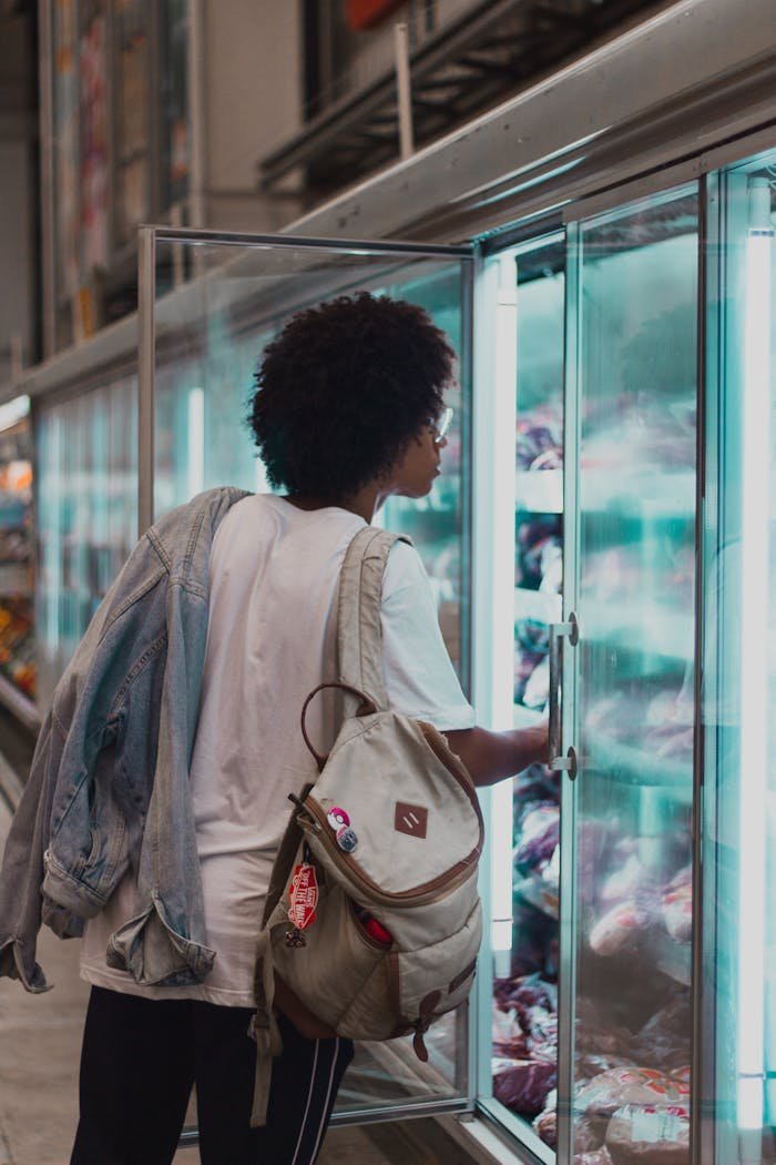 A young person selecting frozen goods in a supermarket aisle.